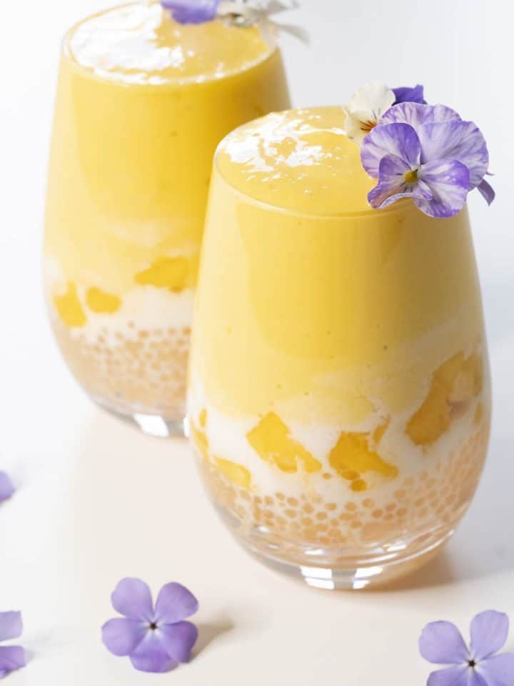 Two mango pomelo sago desserts garnished with purple flowers.
